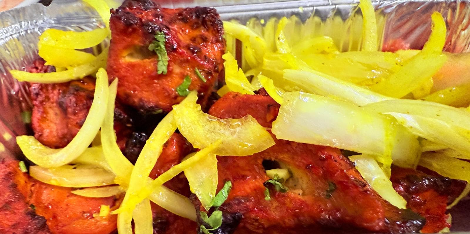 Tandoori paneer in a foil tray, garnished with pickled onion and coriander